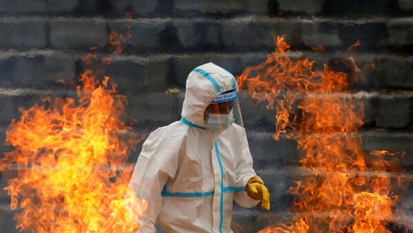 A man wearing personal protective equipment (PPE) walks past the fire as he cremates the bodies of people who died of coronavirus disease (COVID-19), as India's outbreak spreads across South Asia, in Kathmandu, Nepal 5 May 2021.  - Sputnik International