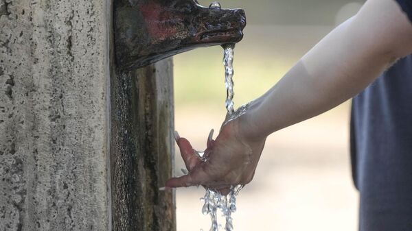A woman puts her hand under water flowing from a fountain with a she-wolf head in Rome, Friday, July 14, 2023. An intense heat wave has reached Italy, bringing temperatures close to 40 degrees Celsius in many cities across the country.  - Sputnik International