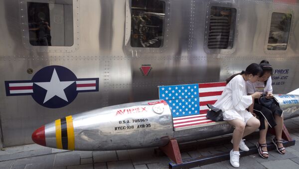 Chinese women look at phone near a rocket shaped bench with an American flag used as a marketing gimmick for a U.S. apparel shop in Beijing, China, Friday, July 6, 2018 - Sputnik International