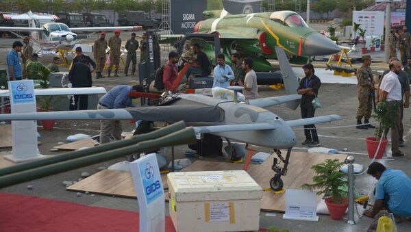 Pakistani officials prepare a locally-manufactured GIDS Shahpar unmanned aerial vehicle for display as a PAC JF-17 Thunder multirole combat aircraft, jointly developed by China and Pakistan, is seen in background at right during preparations for the International Defence Exhibition and seminar (IDEAS) in Karachi on November 29, 2014 - Sputnik International